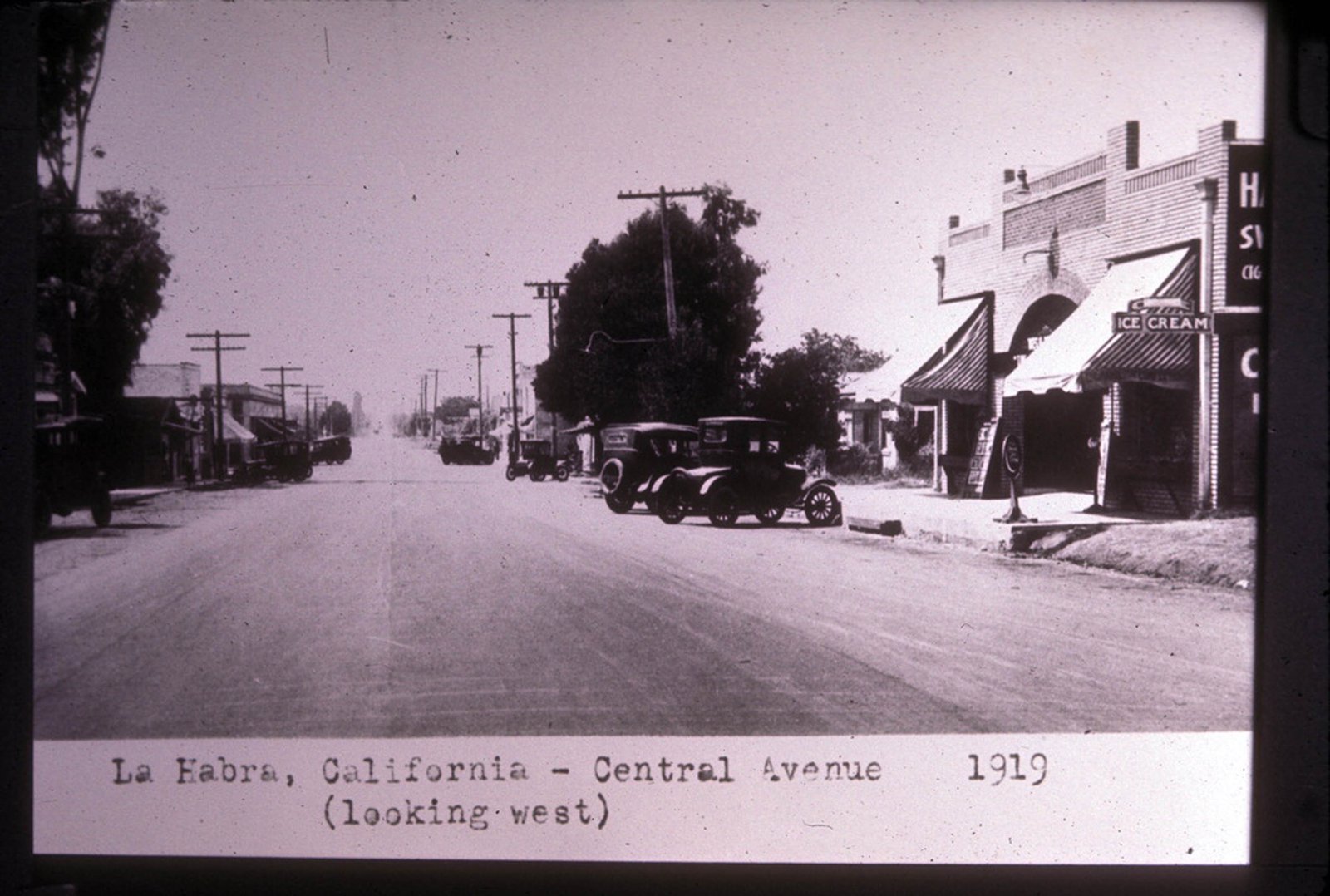 Central Avenue in downtown La Habra, California, looking west, 1919 — storefronts, automobiles, and dirt road.