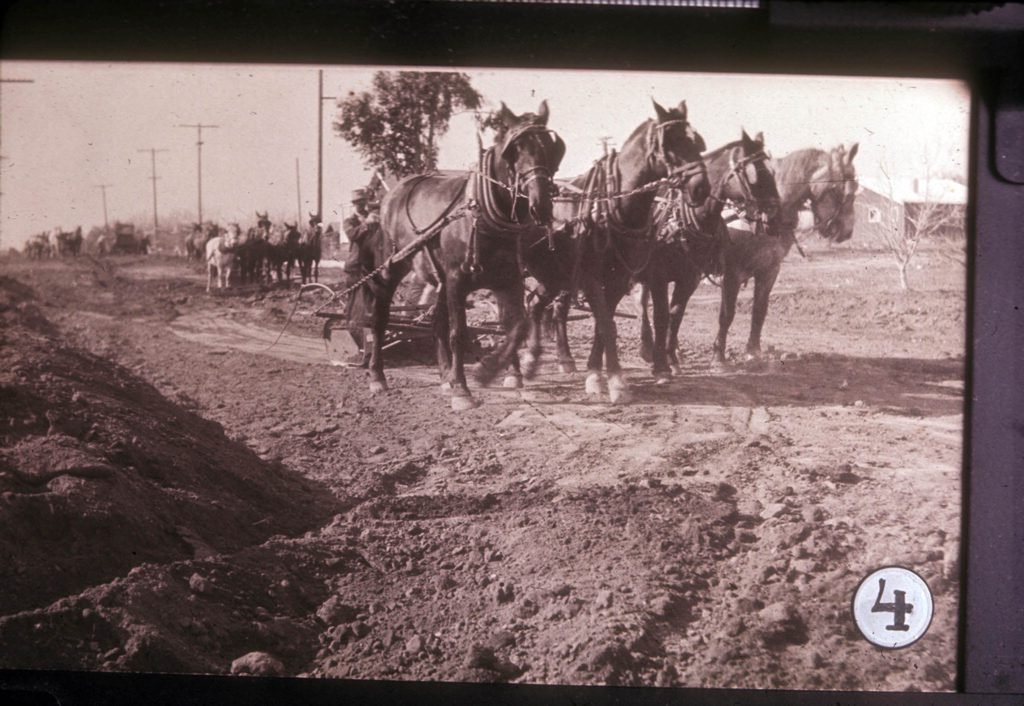 Looking northwest at Central Avenue and shown in the image are teams of horses performing road leveling work.